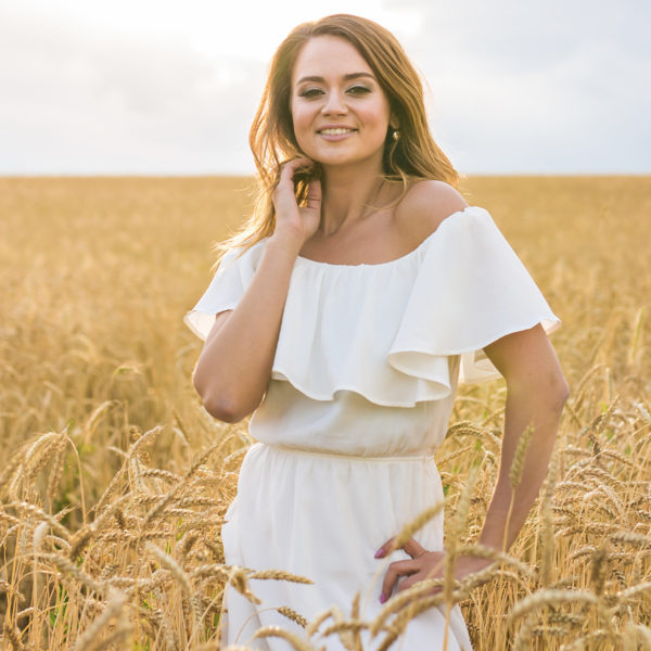 A beautiful woman in a white dress standing in a wheat field after her Breast Lift performed by Dr. Jack Peterson.