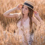A woman in a straw hat sitting in a wheat field, seeking guidance from Dr. Jack Peterson for plastic surgery.