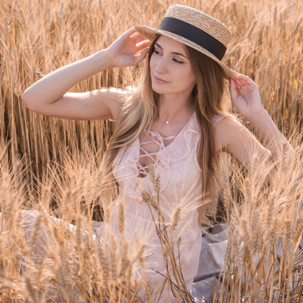 A woman in a straw hat sitting in a wheat field, seeking guidance from Dr. Jack Peterson for plastic surgery.