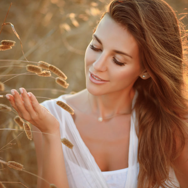 A beautiful woman with Latisse™ Eyelash enhancement in a field with tall grasses, showcasing Dr. Jack Peterson's transformative plastic surgery expertise.