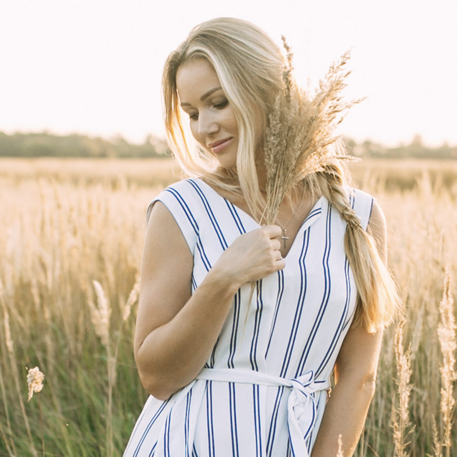 A blonde woman in a striped dress standing in a field undergoing plastic surgery by Dr. Jack Peterson.