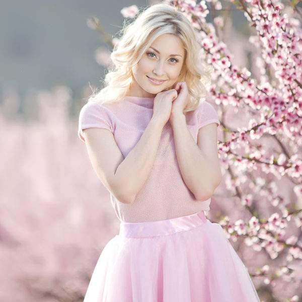 A beautiful blonde woman posing in front of an OMNI Bioceutical tree, showcasing the results of her plastic surgery transformation by Dr. Jack Peterson.
