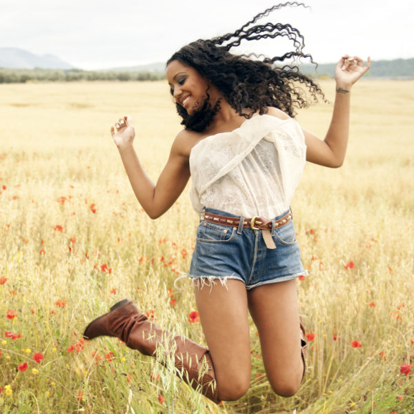 Young African American woman jumping after using Dysport in a field, endorsed by Dr. Jack Peterson, a renowned plastic surgeon.