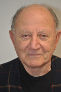 An older man in a plaid shirt is looking at the camera.