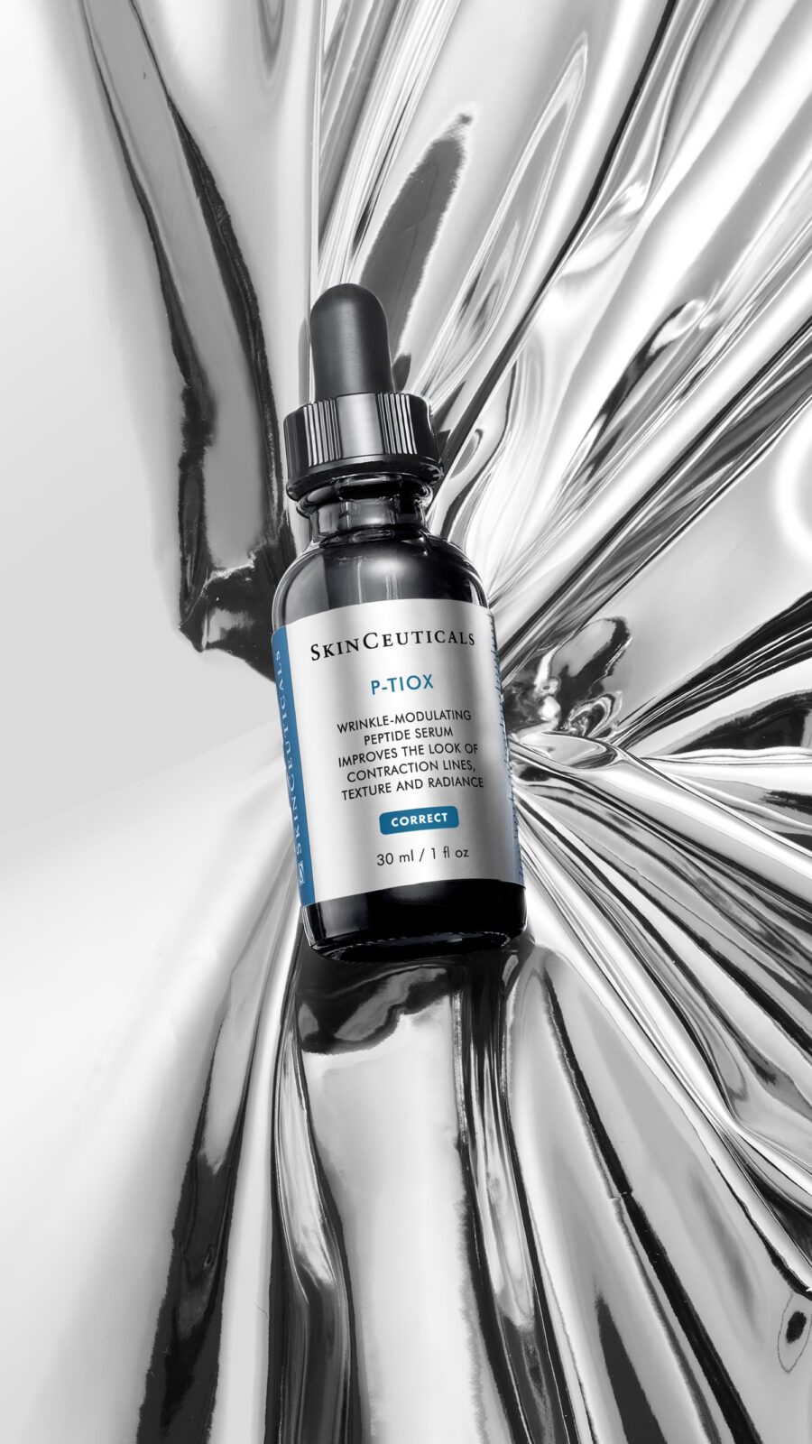 A bottle of SkinCeuticals P-TIOX serum, equipped with a dropper and containing 30ml of product, is placed against a metallic, reflective backdrop.