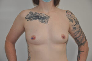 A person with tattoos on their chest and arms is standing topless, facing forward, wearing a mask.