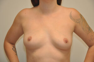 A topless person with tattoos on both arms stands against a plain background, shown from the shoulders to the waist.