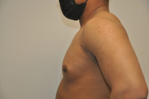 A shirtless person wearing a black face mask stands in profile against a plain background.