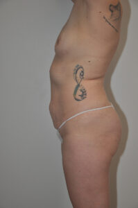 A person standing in profile against a plain wall, wearing white underwear, with visible tattoos on the torso and upper arm.