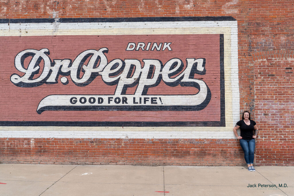 A person stands in front of a large painted brick wall advertisement that reads, 