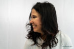 Woman with long dark hair smiling and looking to her left against a plain white background, showcasing the natural results of the best cosmetic injectables for lips.